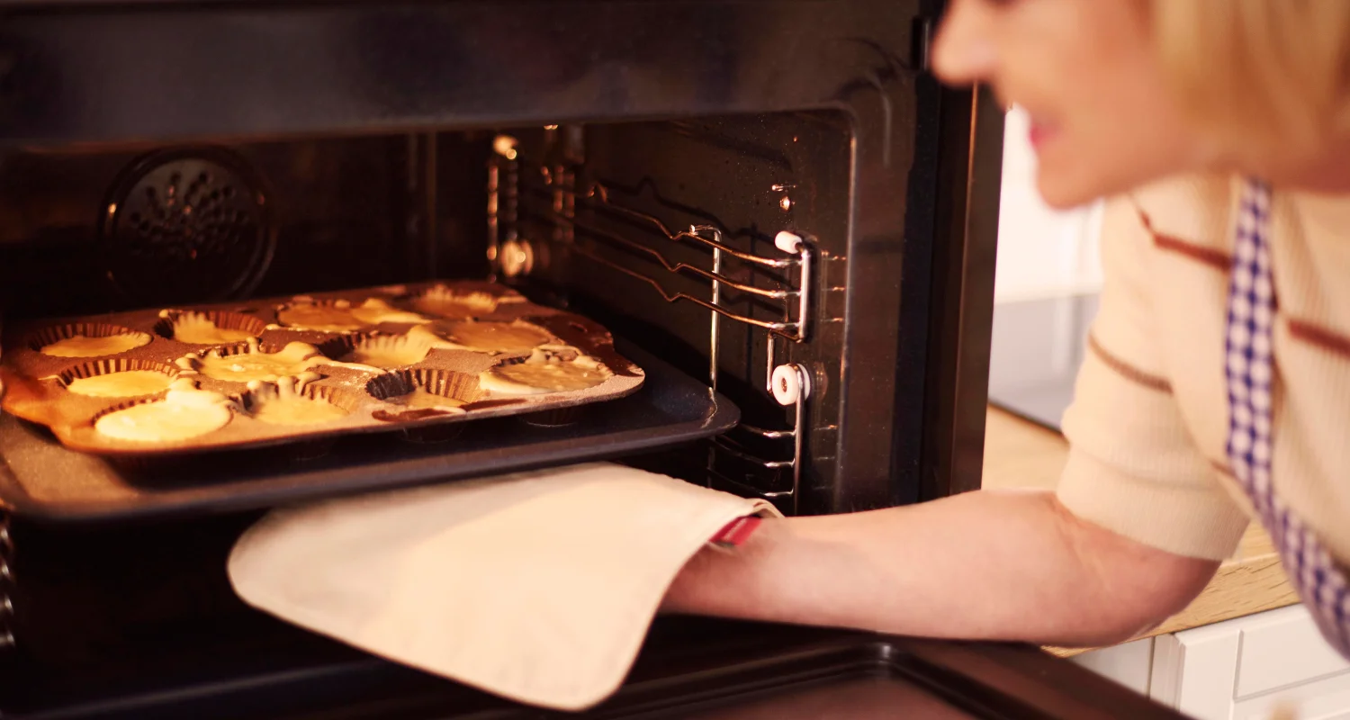 Close-up of a thermometer in puff pastry dough with a baker adjusting the knobs of a vintage oven in the background.