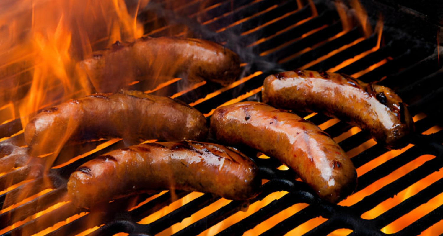 Hands of a cook preparing sausages with fresh herbs, garlic, and spices on a wooden kitchen counter, showcasing the ingredients and tools used in the preparation process.