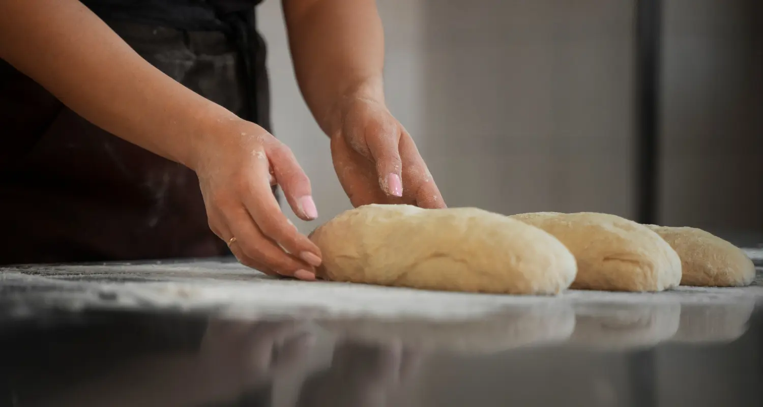 Close-up of a baker's hands using a rolling pin to laminate dough, a crucial technique in making puff pastry.