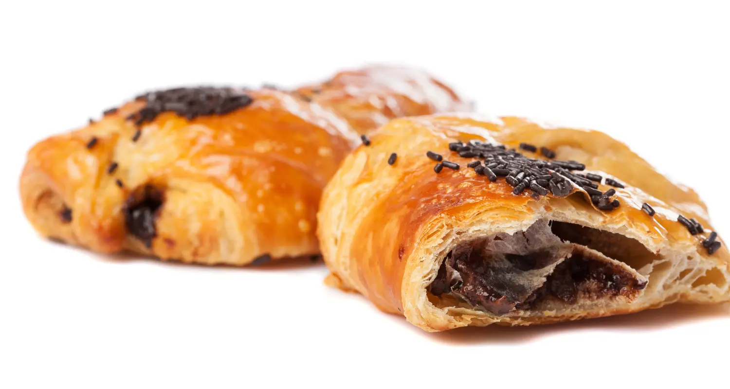 Golden-brown, flaky croissant oozing with Nutella, garnished with a dark chocolate drizzle and scattered chocolate shavings, showcasing a tempting Nutella filled pastry.