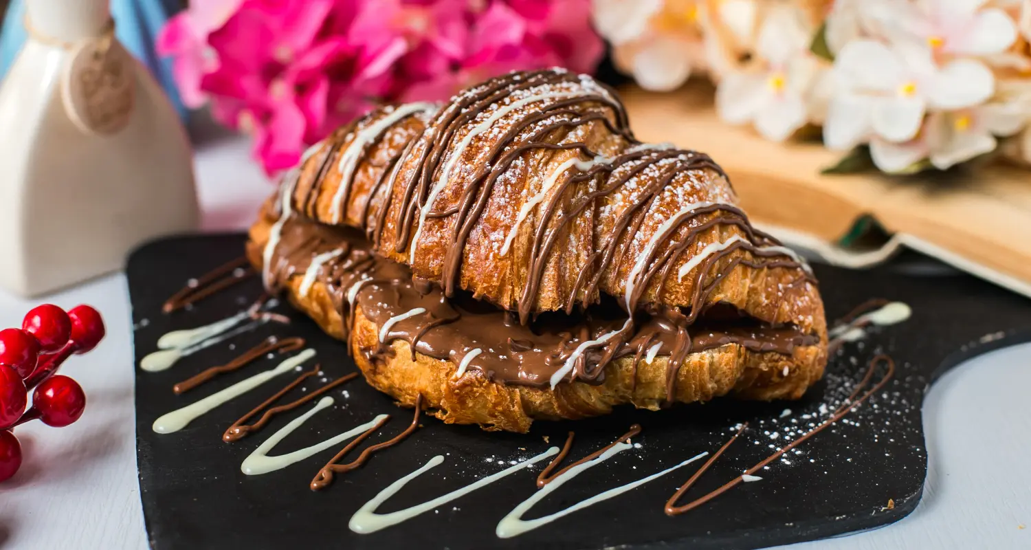 A delectable croissant adorned with chocolate icing and drizzle, a perfect treat for chocolate lovers.